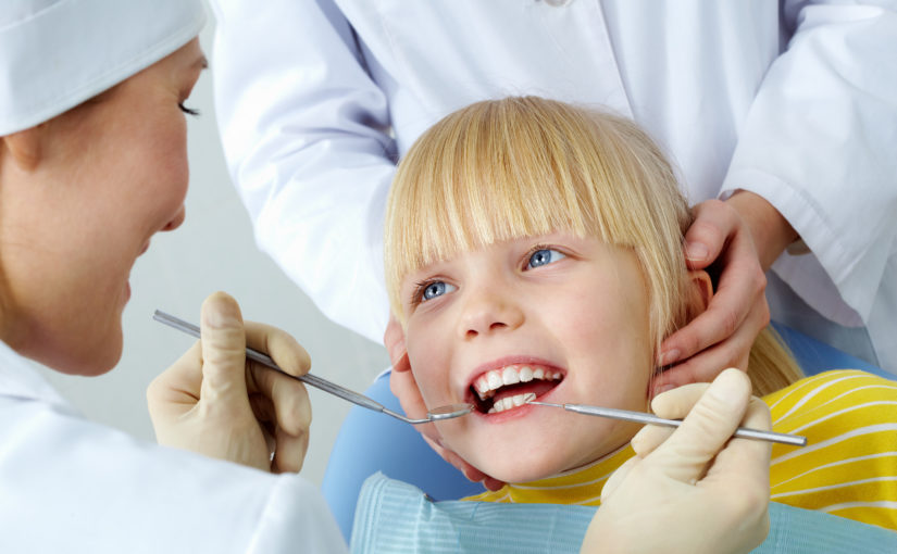 Image of little girl having her teeth checked by doctor and assistant